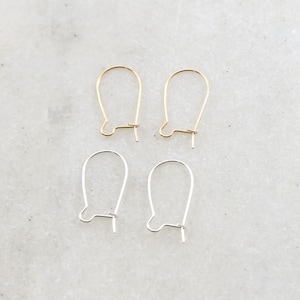 May include: Four earring hooks, two gold and two silver, on a white marble surface.