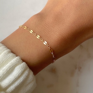 May include: A delicate gold chain bracelet with oval-shaped links. The bracelet is shown on a person's wrist.
