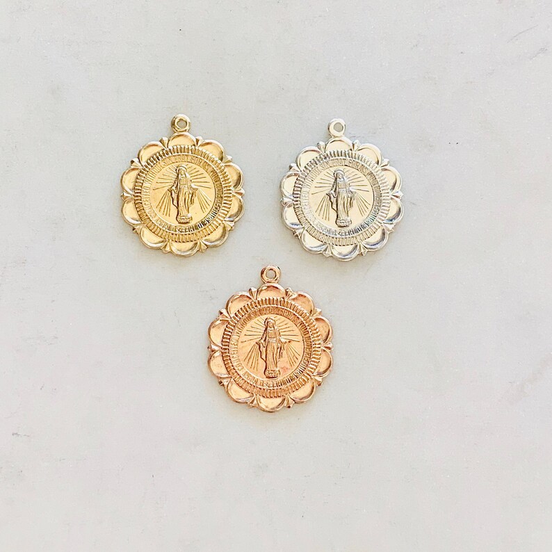 May include: Three gold-toned medallions with a raised image of the Virgin Mary. The medallions have a scalloped edge and are on a white background.