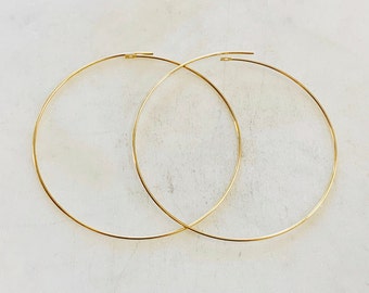 May include: A pair of gold hoop earrings. The hoops are thin and delicate, and they are made of a smooth metal.