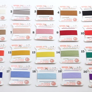May include: A collection of twenty spools of Griffin Natural Silk thread in various colors. Each spool is labeled with the text "NATURAL SILK" and "For stringing pearls and beads". The thread colors include white, gray, brown, black, and shades of red, pink, yellow, green, blue, and purple.