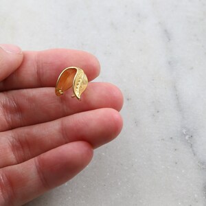 Puede incluir: Cierre de colgante en forma de hoja de oro para la elaboraci&oacute;n de joyas. El cierre est&aacute; hecho de metal y tiene un acabado liso y pulido.