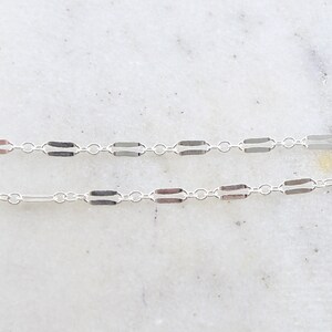 May include: A silver chain necklace with a delicate, box chain design. The chain is made of small, rectangular links that are connected together to create a continuous chain.