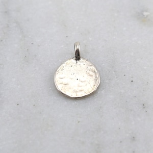 Puede incluir: Un amuleto de plata en forma de círculo con una superficie texturizada.