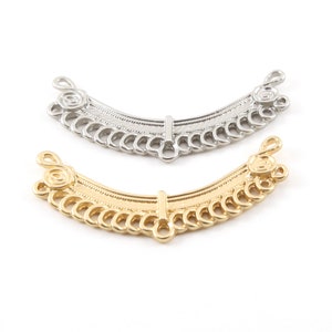 May include: Two metal jewelry connectors, one silver and one gold, with a decorative design of interlocking circles and a central bar. The connectors are shaped like a curved arch.