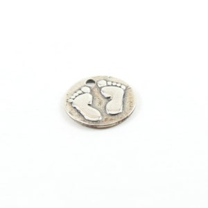 May include: A silver charm in the shape of a circle with two baby footprints embossed on it.
