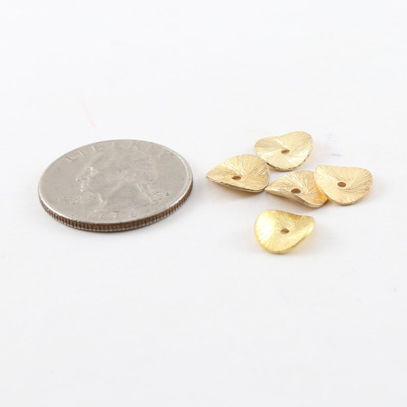 Puede incluir: Cinco cuentas de metal de forma triangular de color dorado con un agujero en el centro. Las cuentas son texturizadas y tienen un acabado ligeramente martillado. Las cuentas son aproximadamente del tama&ntilde;o de una moneda de 25 centavos de d&oacute;lar estadounidense.
