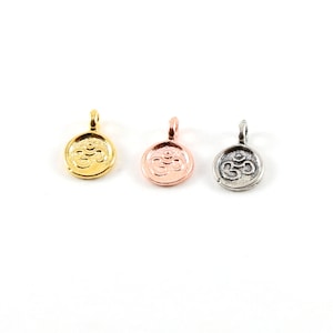 May include: Three Om symbol charms in gold, rose gold, and silver finishes. Each charm is a round disc with a raised Om symbol.
