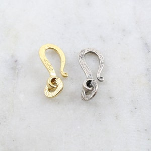 Peut inclure: Deux fermoirs &agrave; crochet en m&eacute;tal, l'un dor&eacute; et l'autre argent&eacute;, sont pr&eacute;sent&eacute;s sur une surface en marbre blanc. Les fermoirs ont une finition textur&eacute;e et un design incurv&eacute;, id&eacute;al pour la fabrication de bijoux ou les projets d'artisanat.
