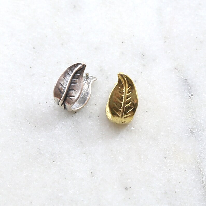 Puede incluir: Dos pendientes en forma de hoja, uno plateado y otro dorado, con un dise&ntilde;o de hoja detallado.