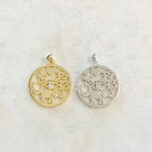 May include: Two pendants, one gold and one silver, with a circular design featuring a heart, a four-leaf clover, a horseshoe, an eye with a single diamond, an elephant, and the number 13.