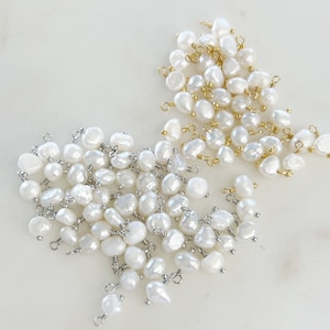 Puede incluir: Un montón de perlas de agua dulce blancas con anillas de salto doradas y plateadas. Las perlas son de forma y tamaño irregulares.