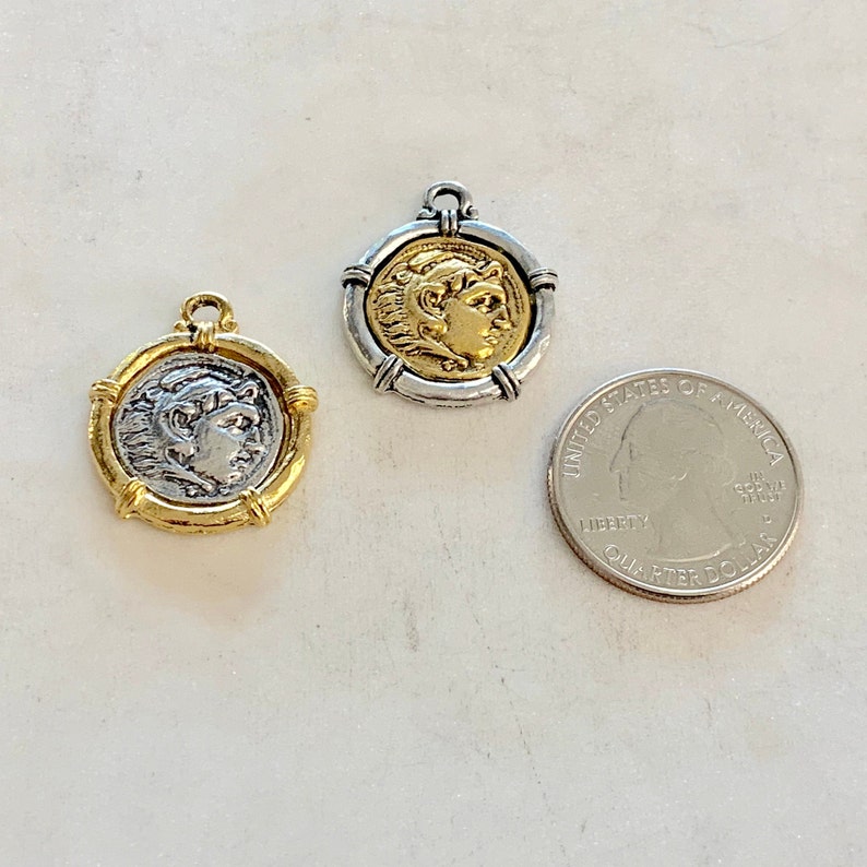 May include: Two gold and silver coin pendants with a profile image of a person on each. The pendants are about the size of a UK 20 pence coin.