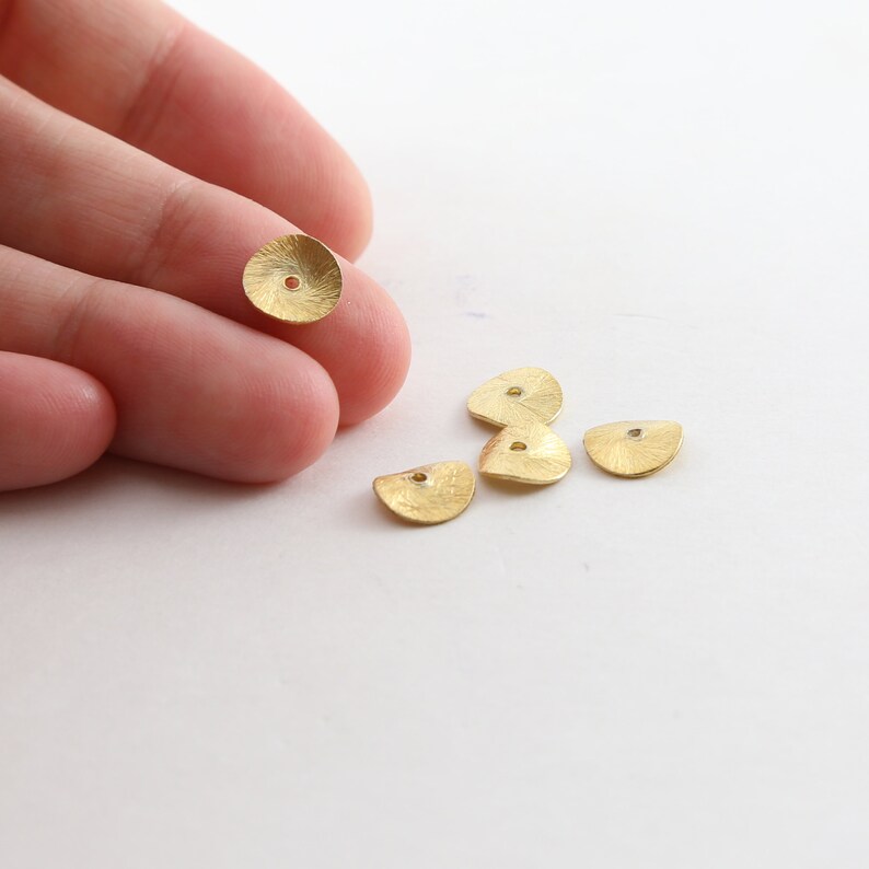 May include: Five gold-colored metal discs with a hole in the center. The discs are slightly domed and have a textured surface.