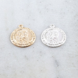May include: Two round metal pendants with a raised image of a saint. One pendant is gold and the other is silver.