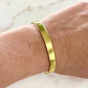 May include: A simple gold-toned metal bracelet. The bracelet is flat and has a smooth, polished finish.