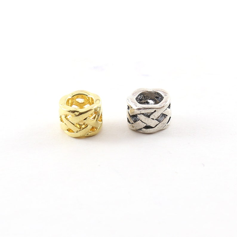May include: Two metal beads with a woven design. One bead is gold and the other is silver.
