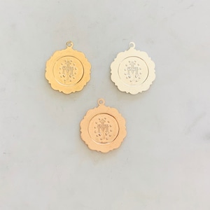 May include: Three gold-toned metal charms with a raised design of the Virgin Mary and a cross. The charms are round and have a scalloped edge.