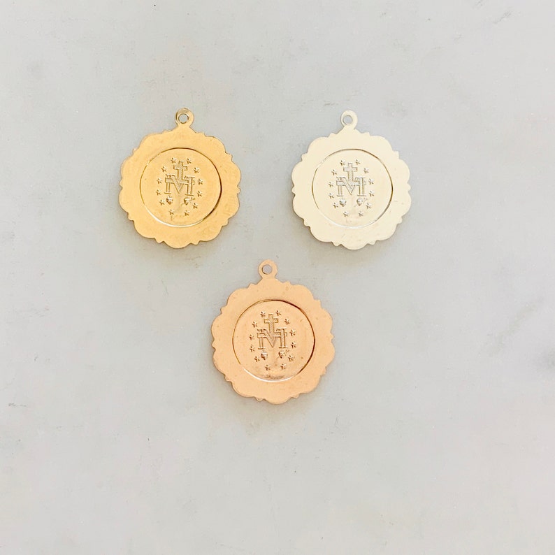 May include: Three gold-toned metal charms with a raised design of the Virgin Mary and a cross. The charms are round and have a scalloped edge.