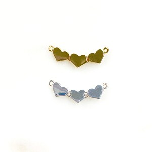 May include: Two heart-shaped jewelry connectors. One is gold-colored, and the other is silver-colored. Each connector has three hearts linked together with small loops on each end.