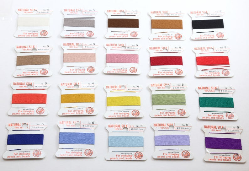 May include: A collection of spools of natural silk thread in various colors, including white, gray, brown, pink, red, orange, yellow, green, blue, and purple. Each spool is labeled with "NATURAL SILK" and "For stringing pearls and beads."
