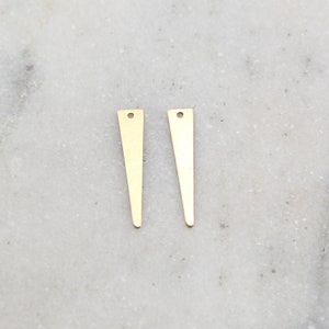 Könnte beinhalten: Zwei goldfarbene Metalldreiecke mit einem Loch oben. Die Dreiecke sind unten spitz und haben eine glatte, glänzende Oberfläche.