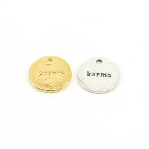 May include: Two round metal charms with the word "karma" engraved on them. One charm is gold and the other is silver.