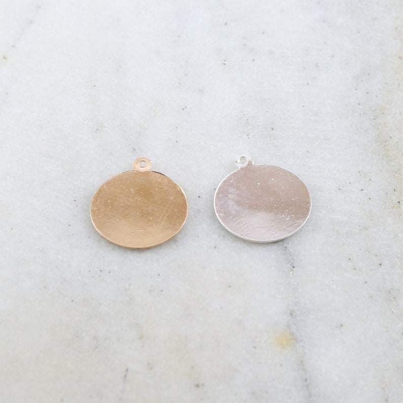 May include: Two round metal charms, one gold and one silver, with a small loop at the top for attaching to jewelry or other crafts.