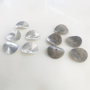 May include: Ten silver-colored metal flower-shaped embellishments with a hole in the center. The embellishments are arranged in two rows of five.