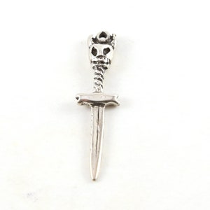 Może przedstawiać: Srebrny wisiorek w kształcie miecza z czaszką na górze. Miecz ma skręcony uchwyt i ostry czubek.