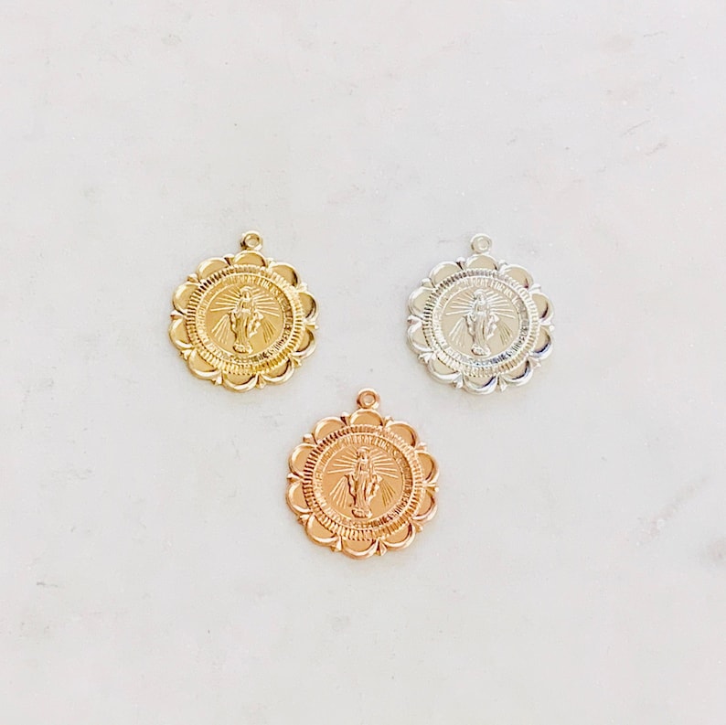 May include: Three gold-toned pendants featuring a religious image of a person with their arms raised. The pendants are round and have a scalloped edge.