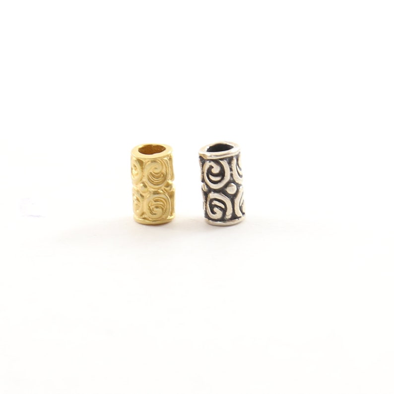 May include: Two decorative hair beads, one gold and one silver, with a swirling pattern.
