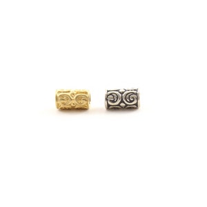 May include: Two metal beads with a decorative swirl pattern. The bead on the left is gold and the bead on the right is silver.