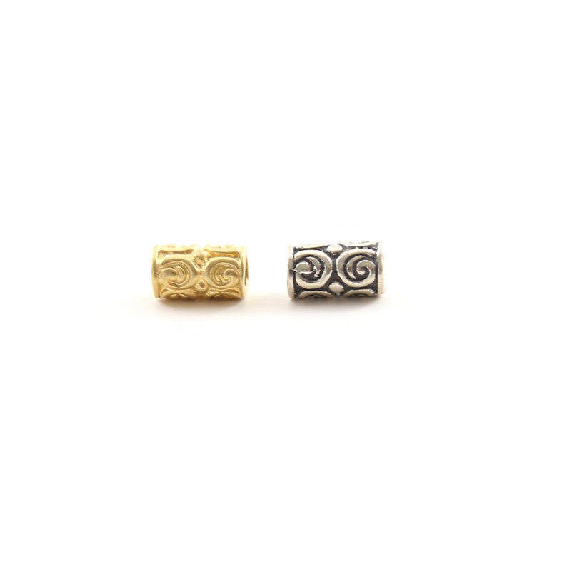 May include: Two metal beads with a decorative swirl pattern. The bead on the left is gold and the bead on the right is silver.