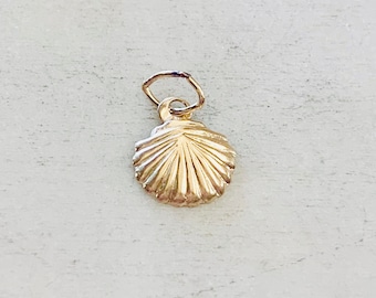 Op de afbeelding: Een gouden schelpbedel met een lus om aan een ketting of armband te bevestigen.