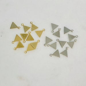 May include: A collection of gold and silver triangle-shaped charms with a loop at the top. The charms are scattered on a white surface.