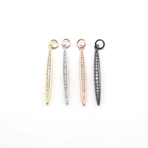 May include: Four pendant charms with a long, thin, oval shape. Each charm is adorned with a row of clear cubic zirconia stones and has a gold, silver, rose gold, or black finish.