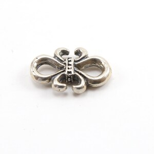 May include: Silver charm in the shape of a stylized butterfly with a decorative band in the center.