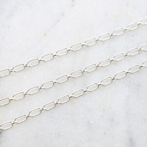 May include: A silver chain necklace with a delicate, oval-shaped link design. The chain is laid out on a white marble surface.