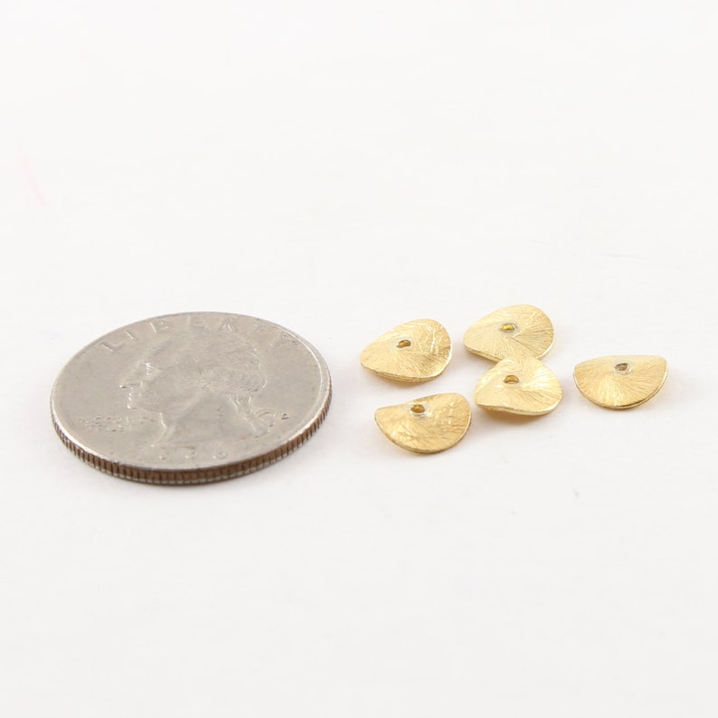 May include: Five gold-colored metal beads with a hole in the center. The beads are shaped like half circles and have a textured surface. The beads are about the size of a US quarter.