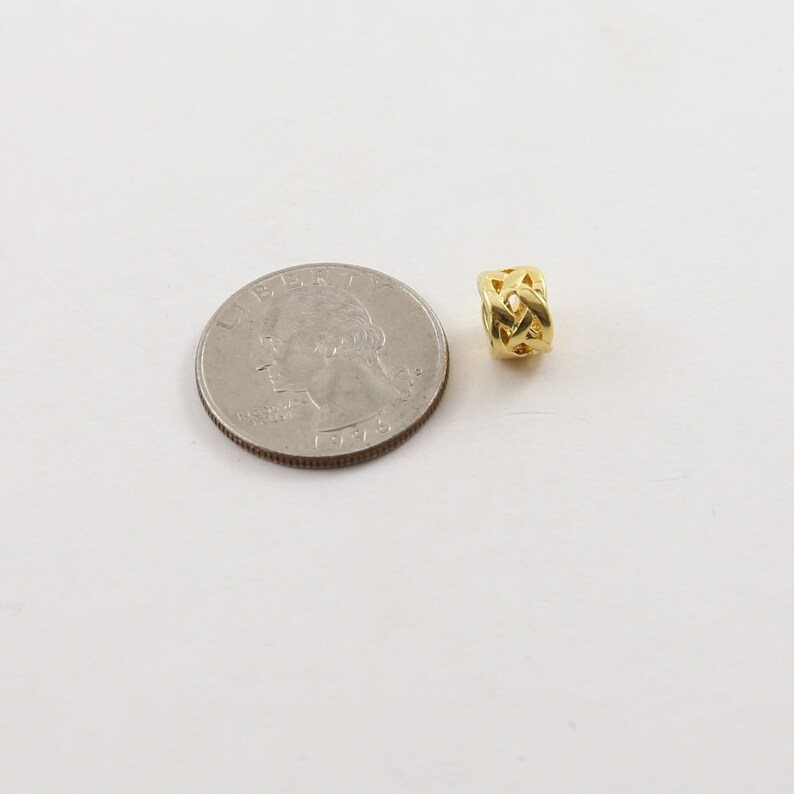 May include: A gold-colored metal bead with a braided design. The bead is about the size of a US quarter.