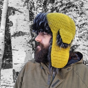 May include: A yellow crocheted trapper hat with a black fur trim. The hat has a large ear flap on one side and a smaller ear flap on the other side.
