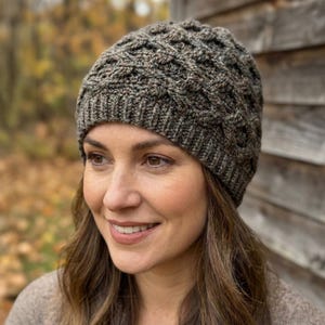 May include: A knitted beanie in shades of brown and gray. The hat features a textured cable knit design and a ribbed brim. The beanie is made of a soft, warm material, perfect for cold weather. The hat is shown on a person.