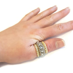 Puede incluir: Un anillo de oro y plata con un diseño de cadena. El anillo se lleva en el pulgar de una mano.