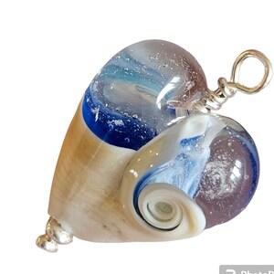May include: A heart-shaped glass pendant with a swirl design in shades of blue, white, and brown. The pendant has a silver bail and is attached to a silver chain.