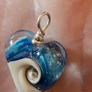 May include: A heart-shaped glass pendant with a swirl of blue and white glass. The pendant has a silver bail and a silver bead at the bottom.