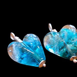 May include: Two blue glass heart-shaped pendants with silver accents. The glass has a swirling, marbled effect.