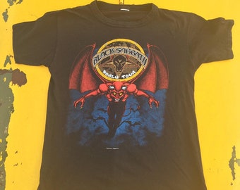 May include: Black Sabbath World Tour t-shirt with a black, red, and yellow graphic of a demon with wings. The graphic is surrounded by a circle with the text "Black Sabbath World Tour".