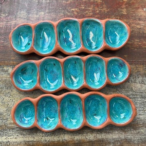 May include: Two terracotta serving dishes with teal blue glaze. Each dish has six individual compartments in the shape of an elongated oval. The dishes are arranged in a staggered pattern.
