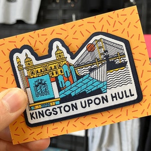 May include: A navy blue patch featuring a colourful illustration of the Kingston upon Hull skyline. The patch depicts a bridge, a building, and a ship. The text "KINGSTON UPON HULL" is printed in white on the patch.